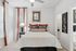 Cozy bedroom with elegant decor, featuring a plush bed with patterned pillows, modern art on the walls, and ample natural light through large windows.