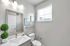 Bright, modern bathroom with sleek fixtures, large mirror, and natural light from window blinds.