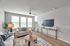 Inviting living room with modern d&eacute;cor, featuring a cozy sofa, stylish round coffee table, and sleek entertainment console, bathed in abundant natural light from large windows.