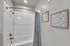 Modern bathroom with elegant white tile shower, stylish framed art, and a chic shower curtain.