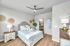 Inviting bedroom with plush bedding, light wood flooring, modern ceiling fan, and elegant decor, seamlessly connecting to a chic bathroom.