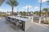 Luxurious outdoor patio with grill, modern seating, and lush palm trees, perfect for entertaining or relaxing in a sunny oasis.
