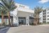 Modern apartment complex entrance with sleek architecture and lush palm trees under a clear blue sky.