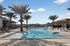 Luxurious outdoor pool area with palm trees, sun loungers, and a modern cabana under a bright blue sky.
