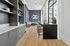 Elegant modern apartment lounge with sleek dark cabinetry, light wood flooring, and a cozy seating area by expansive windows offering abundant natural light.