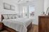 Charming bedroom with elegant decor featuring a cozy bed, stylish wooden furniture, and bright natural light through large windows.