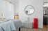 Charming bedroom scene with stylish decor, featuring a cozy bed with a light blue blanket, a trendy round mirror, and a vibrant red accent piece for a modern touch.