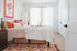 Bright and inviting bedroom with modern decor, boasting natural light, colorful artwork, and cozy bedding against a chic white backdrop.