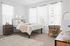 Bright and airy bedroom with modern decor, featuring a comfortable bed, stylish side table, and elegant chair, illuminated by natural light through large windows.