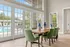 Bright dining room with green chairs, wooden table, and large windows overlooking a pool area.