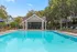Luxurious outdoor swimming pool with a clubhouse surrounded by lush greenery and sun loungers.