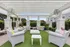 Chic outdoor seating area with white furniture under a stylish pergola, surrounded by greenery.