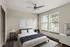 Bright and modern bedroom with a large bed, sleek ceiling fan, and natural light streaming through two large windows.