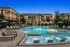 Elegant apartment complex featuring a sparkling swimming pool with lounge chairs and umbrellas.