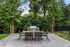 Inviting outdoor patio with dining set, grill, and string lights under lush greenery.