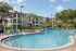 Vibrant apartment complex featuring a sparkling pool with palm trees and modern lounge chairs.