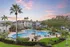 Luxurious apartment complex featuring a central swimming pool, surrounded by palm trees and well-maintained greenery at sunset.
