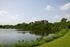Tranquil lakeside scene featuring calm water and lush green foliage under a bright blue sky.