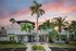 Elegant residential complex entrance with palm trees at sunset, featuring modern architecture and lush landscaping.
