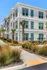 Modern three-story apartment building with large windows, surrounded by palm trees and landscaped pathways.