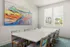 Elegant dining room with a modern white table, colorful chairs, and vibrant landscape painting.