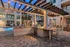 Charming outdoor patio area with a modern grill and string lights near a swimming pool and apartment complex.