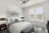 Elegant bedroom featuring a plush bed, contemporary artwork, and two large windows with ample natural light.