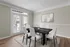 Elegant dining room with a modern black table and six white chairs, featuring large windows for natural light and a stylish wall painting.
