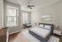 Elegant bedroom featuring a plush bed with modern side tables, a stylish armchair by large windows, and a serene landscape painting on the wall, creating a tranquil atmosphere.