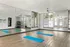 Modern fitness studio with mirrored walls, blue yoga mats on wooden floor, and ample natural light.