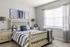 Charming bedroom with elegant decor, featuring a cozy bed, stylish bedside tables with lamps, and artistic wall art in soft blue tones.