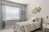 Cozy bedroom with elegant decor, featuring a comfortable bed with patterned bedding, stylish wall art, and soft natural light through sheer curtains.