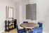 Elegant dining room with a round wooden table and plush blue chairs, featuring modern wall art and a stylish mirror, perfect for intimate gatherings.