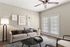Elegant living room with contemporary decor, featuring a comfortable beige sofa, stylish artwork, and large windows with blinds allowing natural light.