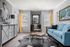 Bright and sophisticated living room featuring a stylish blue sofa, unique natural wood coffee table, elegant wall art, and ample sunlight streaming through large windows with yellow curtains.