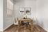 Chic dining area with a rustic wooden table, elegant beige chairs, and modern artwork on white walls.