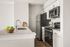 Modern kitchen with sleek stainless steel appliances, elegant white cabinetry, and a spacious marble countertop adorned with a bowl of fresh green apples.
