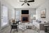 Chic living room with a cozy fireplace, elegant furniture, and a modern ceiling fan, illuminated by natural light through large windows.