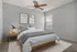 Inviting bedroom with modern decor, featuring a cozy bed, stylish artwork, and sleek ceiling fan, bathed in natural light from a large window.