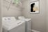 Modern laundry room with sleek washer and dryer, featuring minimalist artwork and practical wire shelving for organized storage.