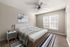 Elegant and cozy bedroom with modern decor, featuring a comfortable bed, stylish artwork, and a ceiling fan, bathed in natural light from a large window.