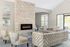 Elegant living room with a modern stone fireplace, plush tufted sofas, and sunlight streaming through large windows, creating a warm and inviting atmosphere.
