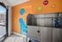 Bright pet spa facility featuring a stainless steel washing station, vibrant orange walls with playful pet-themed decals, and convenient access to the outdoors.