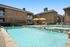 Inviting apartment complex with a sparkling outdoor pool, sun loungers, and bright yellow umbrellas, perfect for relaxation and leisure.