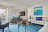 Modern living room with stylish blue accents, featuring a cozy seating area, vibrant abstract art, and an open dining space with patio access.