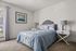 Bright and cozy bedroom featuring a stylish bed with patterned bedding, elegant side tables with lamps, and a captivating wall art piece, perfectly illuminated by natural light from large windows.