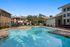 Inviting outdoor pool surrounded by cozy seating, lush greenery, and charming brick buildings under a bright blue sky.