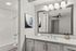 Modern bathroom with elegant white cabinetry, large mirror, and stylish overhead lighting, featuring a pristine bathtub and artistic wall decor.