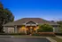 Charming residential building with elegant exterior lighting, surrounded by lush greenery and vibrant flowers at dusk.