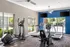 Modern fitness center with treadmills, elliptical, and stationery bike, featuring large windows and blue accent walls.